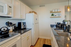 Eine moderne Küche mit weißen Schränken, einem Edelstahl-Kühlschrank, einer Kaffeemaschine und einem Waschbecken mit Granitarbeitsplatte.