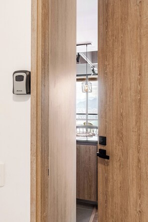 A wooden door leading to a balcony with a hanging light fixture and a view of the cityscape. - One Living Luxe Mall City Plaza (Envigado)