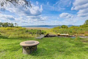 A grassy area with a circular structure, a wooden bridge, and a body of water in the distance. - Lakefront Adirondack Escape! Fire Pit & Game Room (Broadalbin)
