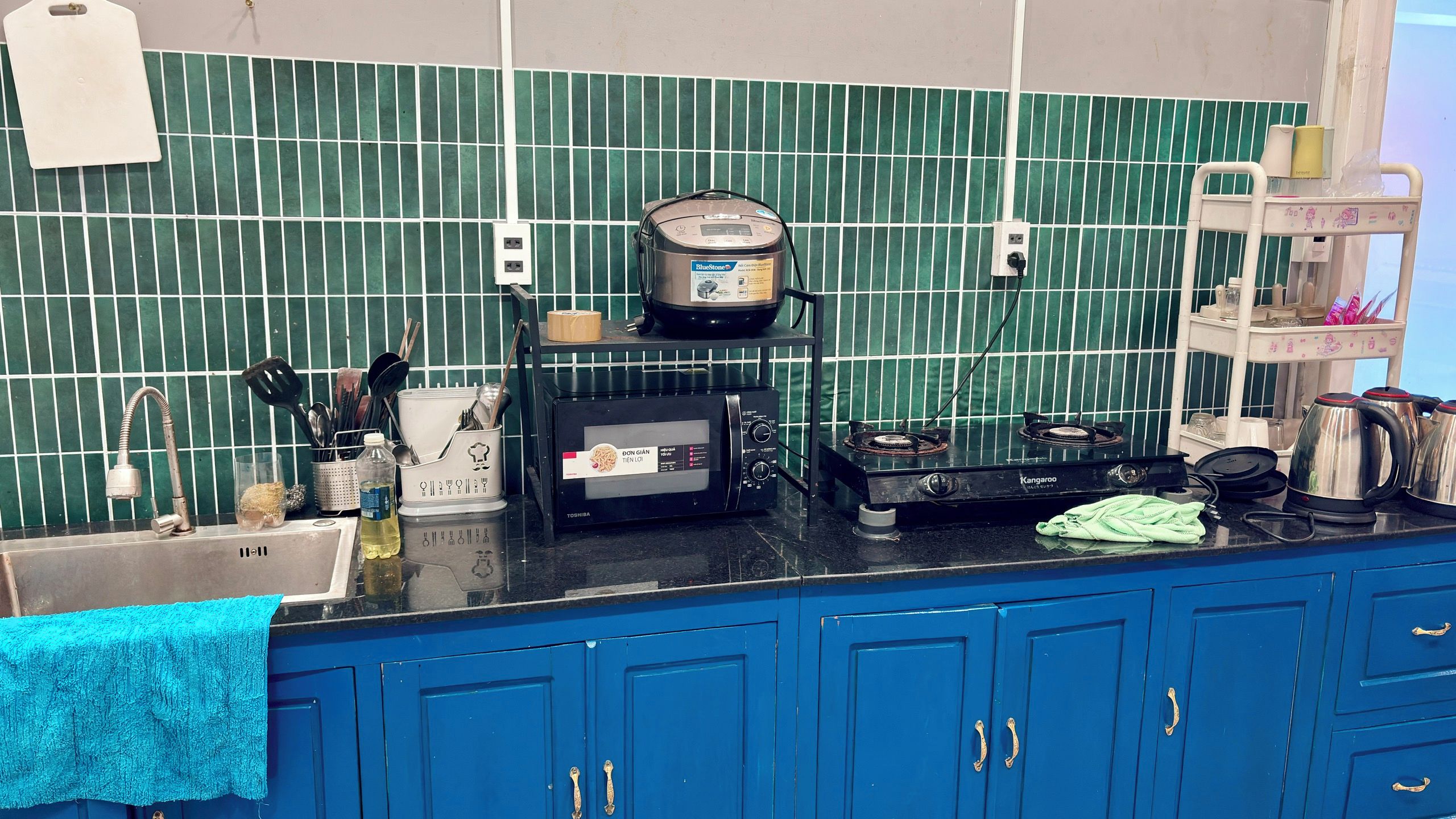 Een keuken met een blauw aanrecht, een rijstkoker, een broodrooster en een waterkoker.