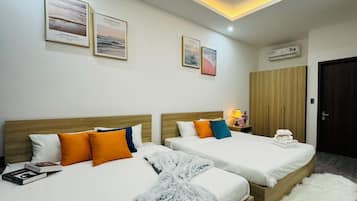 Habitación de hotel con dos camas, un armario, una mesita de noche con lámpara y cuadros en la pared.