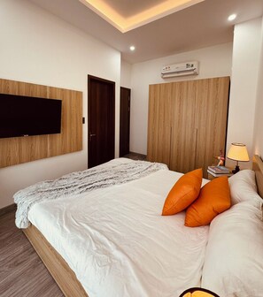 A modern bedroom with a large bed, a mounted TV, a wardrobe, and an air conditioning unit. - Teddy Pumpkin – Grandworld Phu Quoc – Near beach (Phu Quoc)