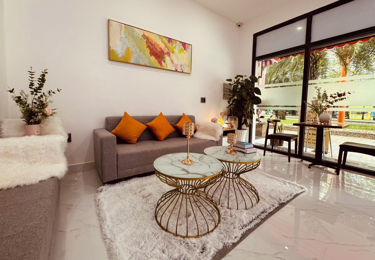 Un salon moderne avec un canapé gris, des coussins orange, deux tables basses surmontées de plateaux en marbre et un tapis à poils longs blanc.