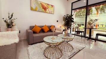 Un salon moderne avec un canapé gris, des coussins orange, deux tables basses surmontées de plateaux en marbre et un tapis à poils longs blanc.