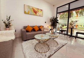 Sala de estar moderna com sofá cinza, almofadas laranja, duas mesas de centro com tampo de mármore e um tapete felpudo branco.