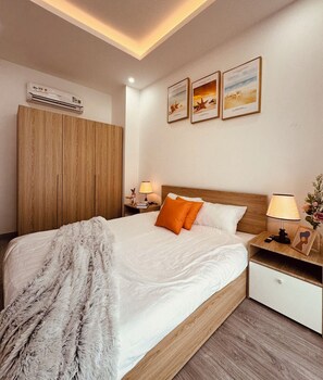 A hotel room with a bed, a wardrobe, a nightstand with a lamp, and framed pictures on the wall.