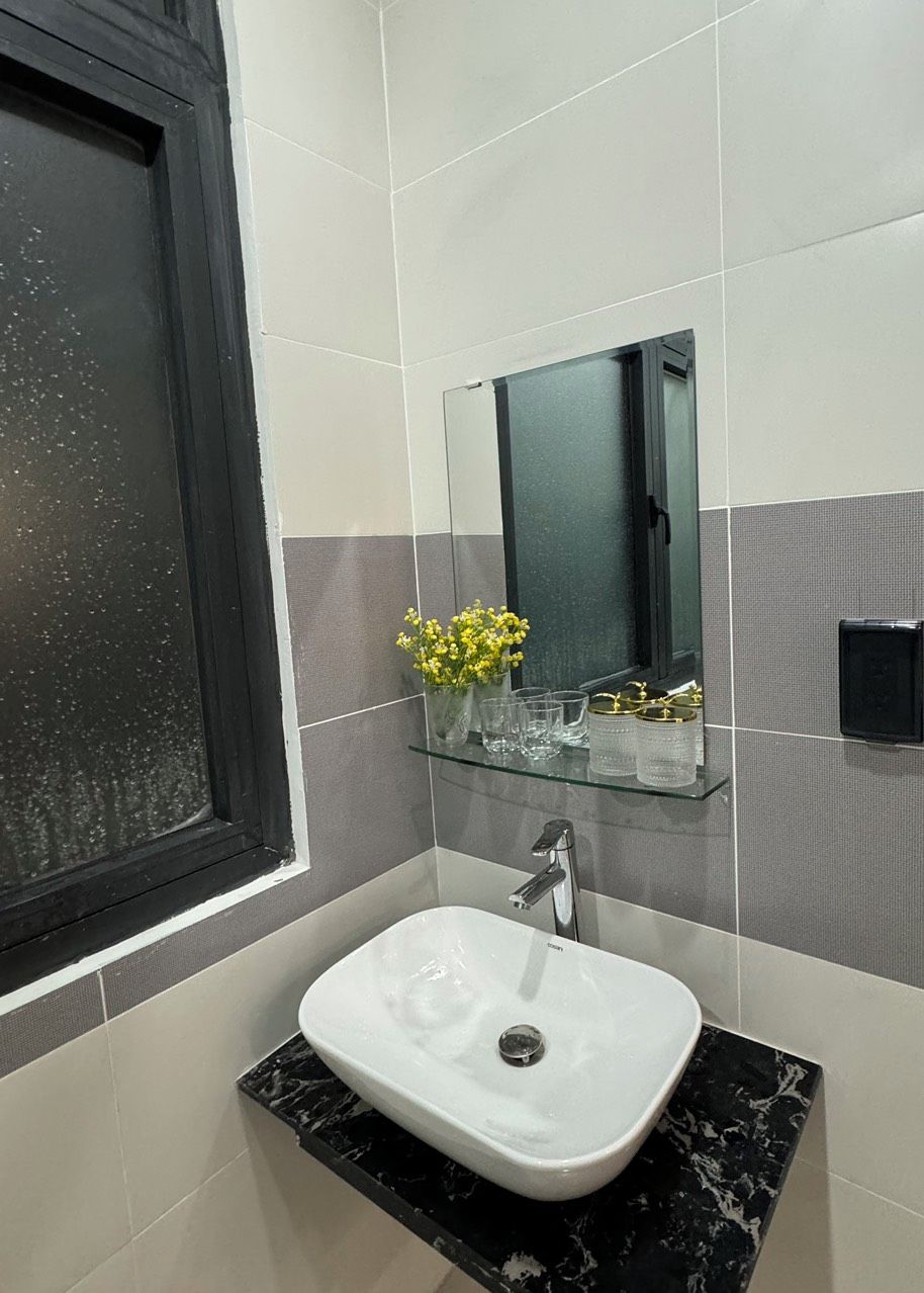 Un baño con un lavabo blanco, una estante de vidrio con objetos decorativos y un espejo sobre el lavabo.