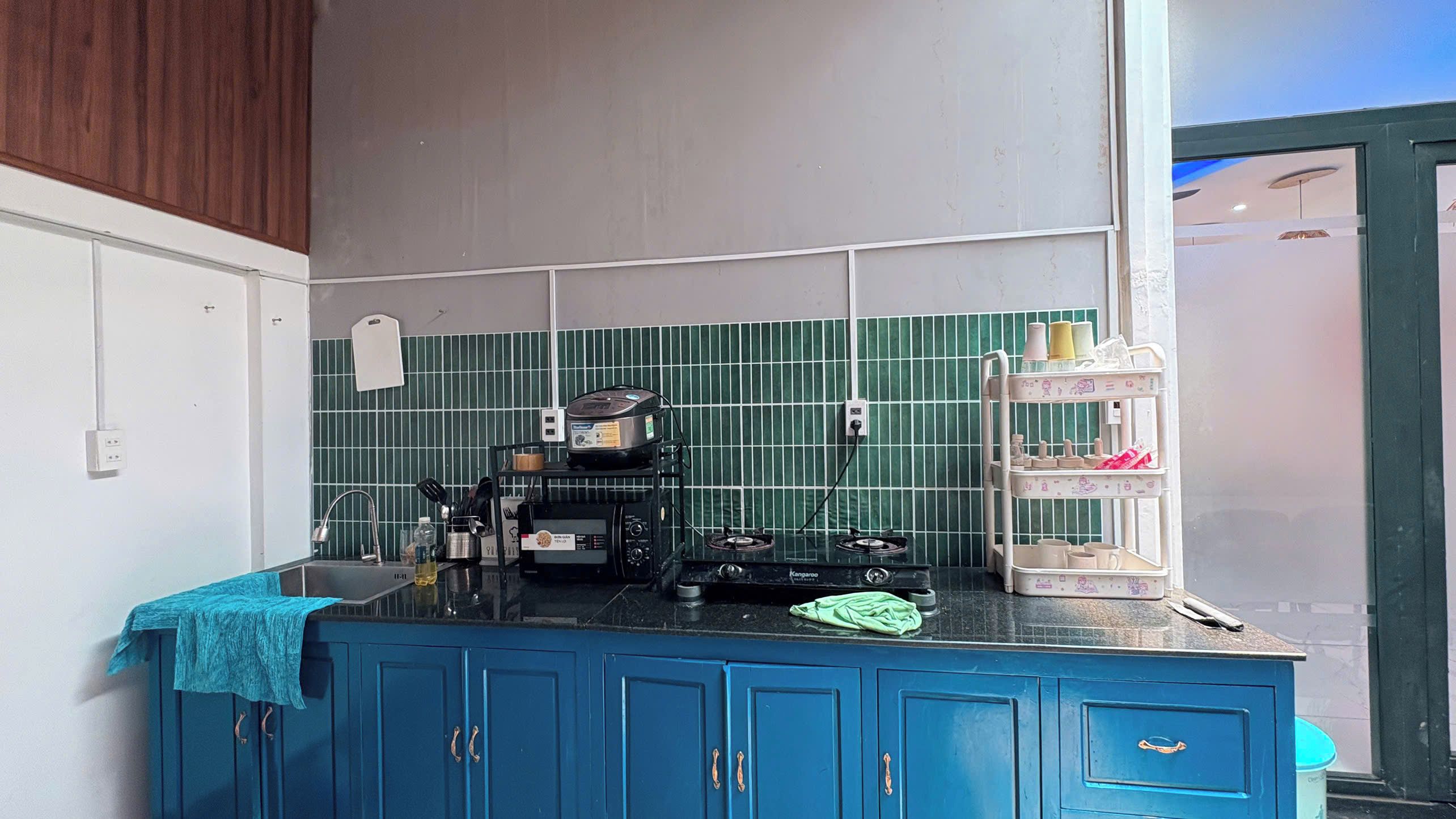 A kitchen with blue cabinets, a gas stove, a coffee maker, and a green tiled backsplash.