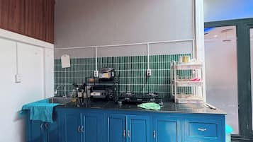 A kitchen with blue cabinets, a gas stove, a coffee maker, and a green tiled backsplash.