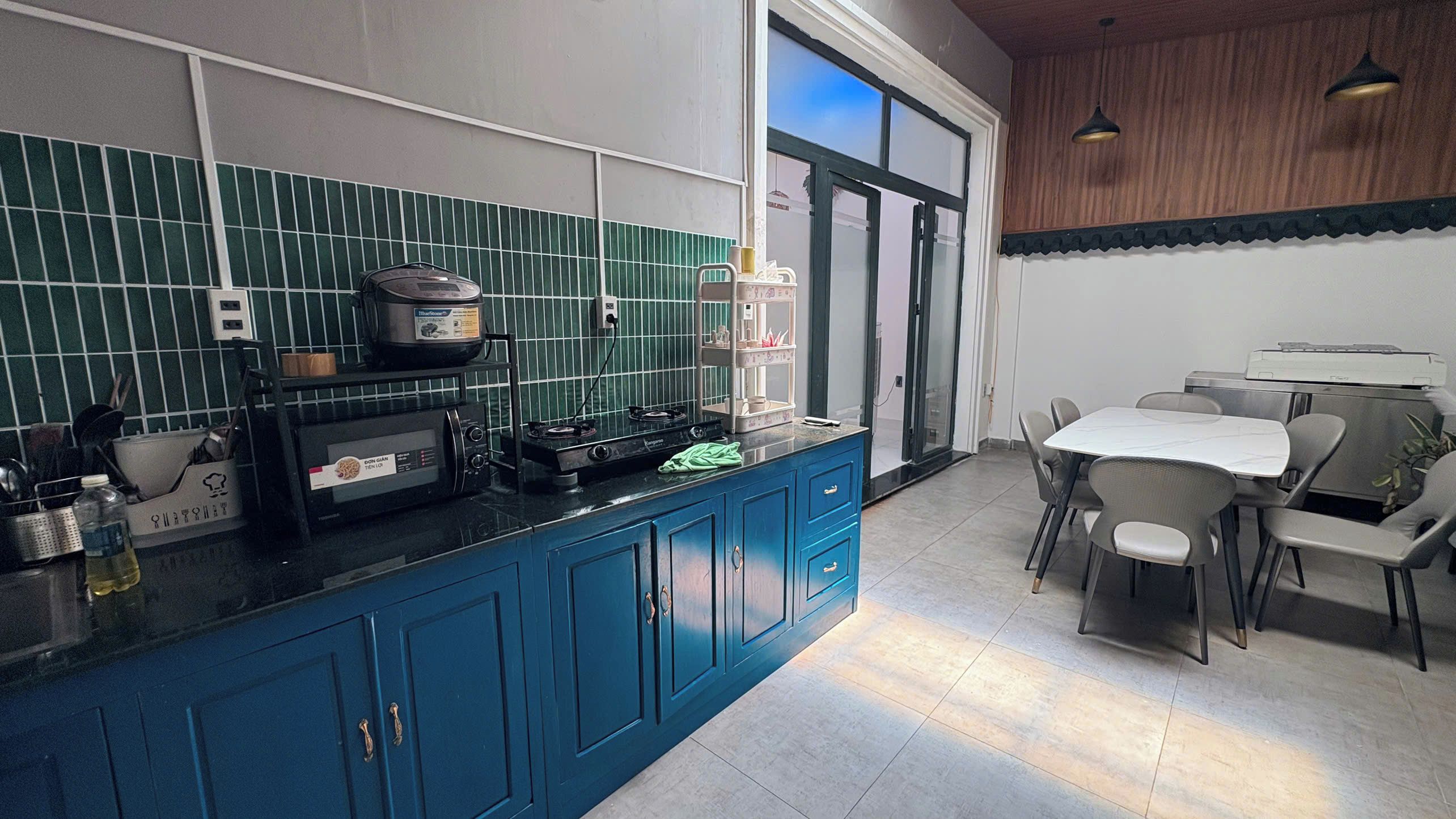 A modern kitchen with blue cabinets, a dining area with a table and chairs, and a large window.