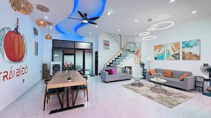 A modern living room with a dining area, a staircase, and a kitchen visible through a glass door. - Teddy Pumpkin – Grandworld Phu Quoc – Near beach (Phu Quoc)