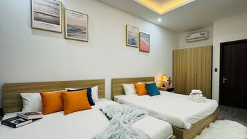 A hotel room with two beds, a wardrobe, a bedside table with a lamp, and framed pictures on the wall.