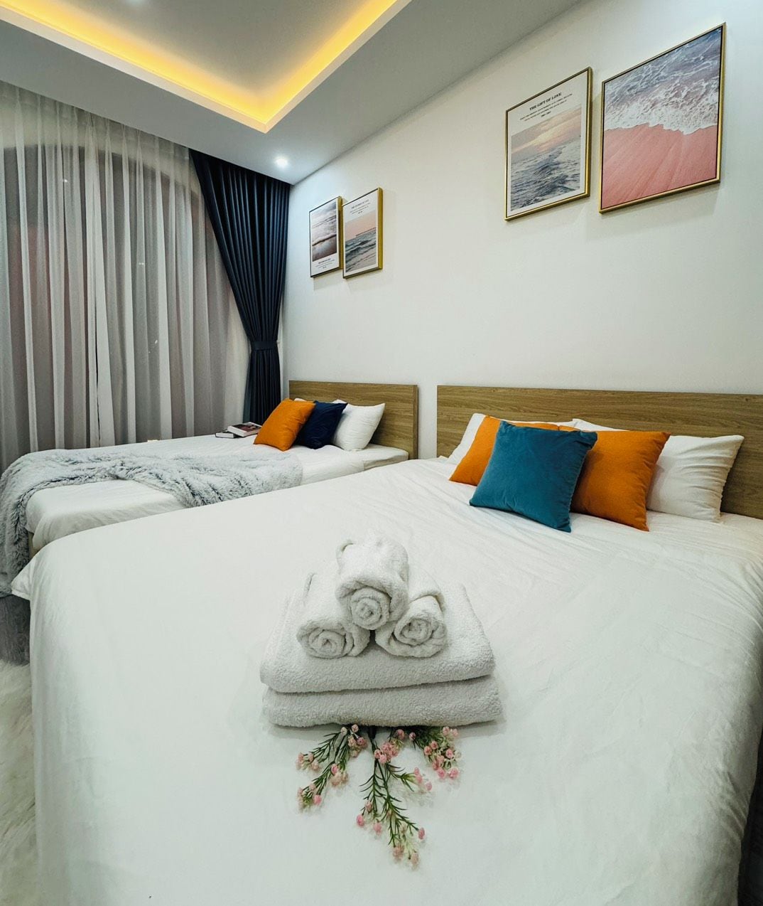 Ein Hotelzimmer mit zwei Betten, einem großen Fenster mit Vorhängen und Bildern an den Wänden.
