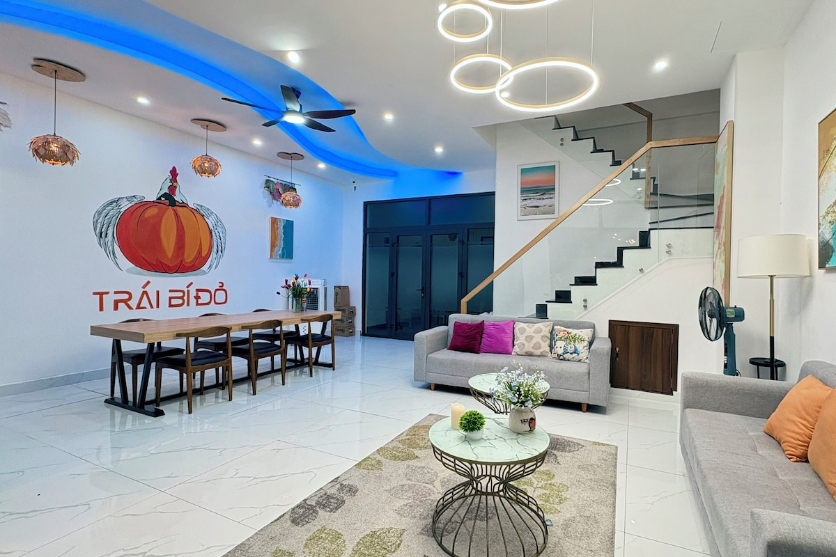 Un salon moderne avec un coin repas, un escalier et une cuisine visible au fond.