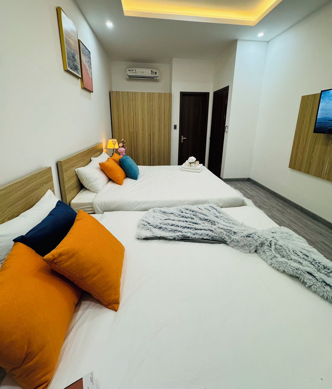 A hotel room with two beds, a flat-screen TV mounted on the wall, and an air conditioning unit.