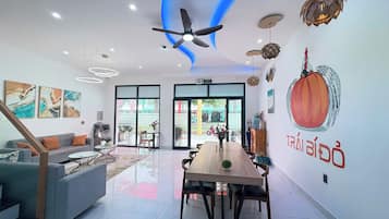 Un espace de vie moderne comprenant un coin repas, un canapé, un ventilateur de plafond et des œuvres d’art accrochées aux murs.