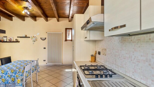 Una cucina con piano cottura a gas, mobili bianchi, zoccolo di piastrelle e soffitto in legno.