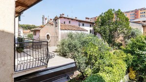Un balcone abitativo con ringhiera in metallo, una piccola area giardino con diverse piante e vista su abitazioni vicine dalle architetture differenti.