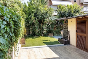 A residential garden with a wooden deck, a small lawn, and a building with a wooden door and shutters. - house verona (Veneto)