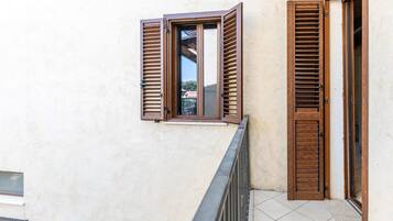 Un balcón con contraventanas de madera, suelo de baldosas y vista a un edificio al fondo.