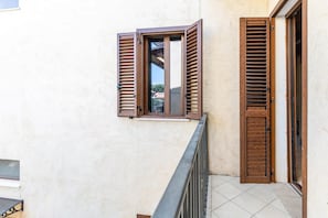A balcony with wooden shutters, a tiled floor, and a view of a building in the background. - house verona (Veneto)