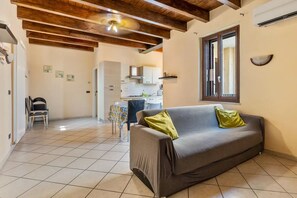 Una sala de estar con sofá, un comedor con mesa y sillas, una cocina al fondo y un techo con vigas a la vista.