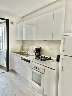 A modern kitchen with white cabinetry, a built-in dishwasher, a coffee maker, and a stove. - Luminous Escape to La Marsa (La Marsa)