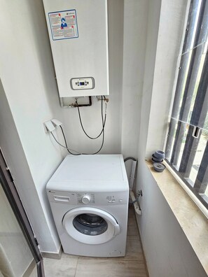 A compact laundry room with a front-loading washing machine, a control panel above it, and a window with a view. - Luminous Escape to La Marsa (La Marsa)