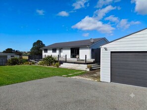 A residential property with a two-story house, a garage, and a well-maintained lawn. - Pukehina Retreat: 
Private Pool, Pastures & Beach. (Pukehina)