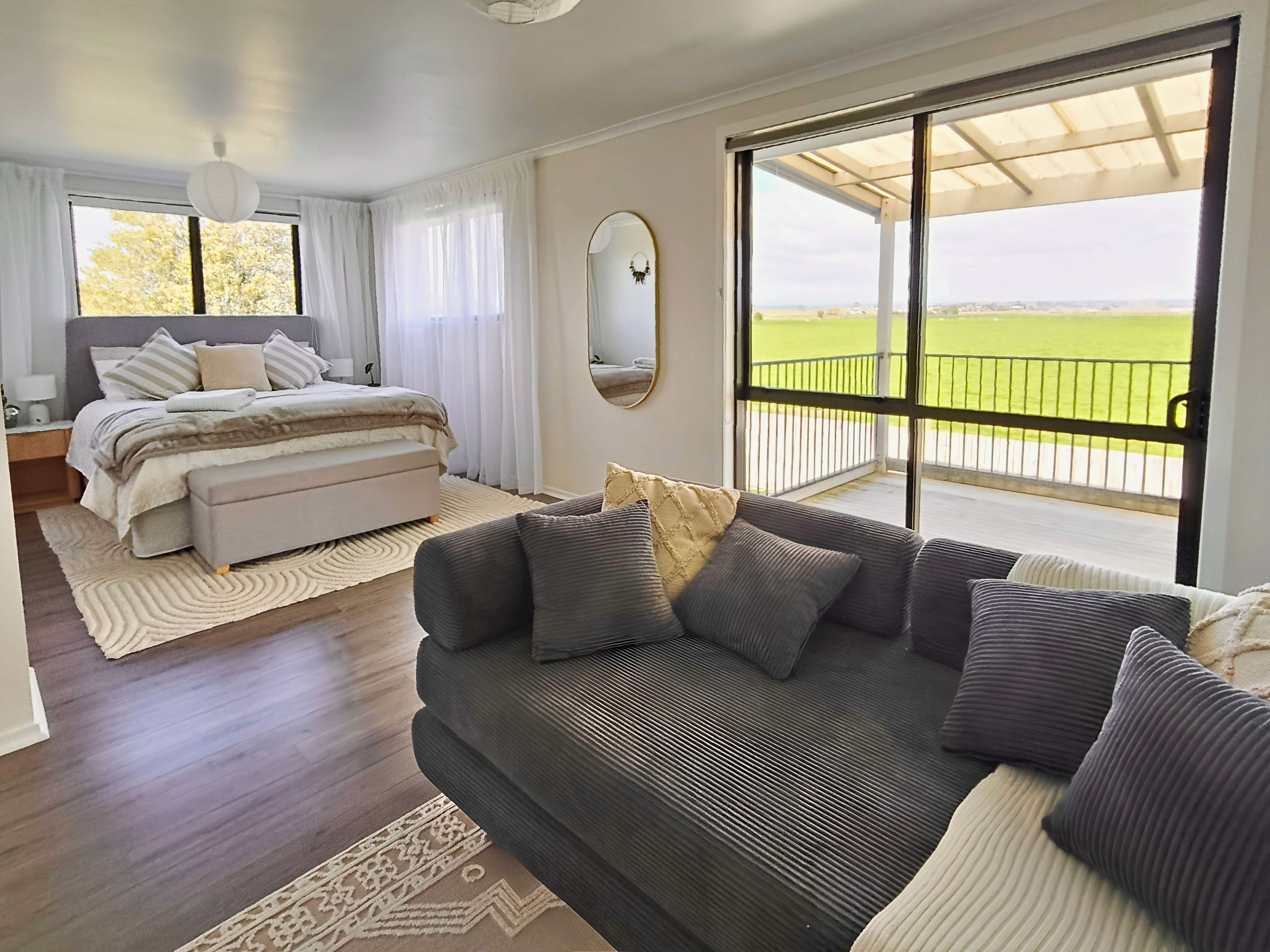 A bedroom with a bed, a sofa, a large window with a view, and a ceiling fan.
