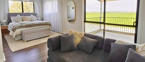 A bedroom with a bed, a sofa, a large window with a view, and a ceiling fan.