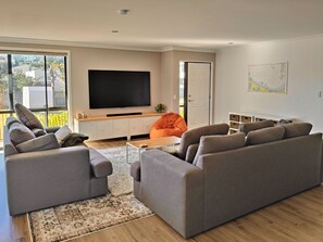 A modern living room with grey sofas, a flat-screen TV, a coffee table, and a patterned rug. - Pukehina Retreat: 
Private Pool, Pastures & Beach. (Pukehina)