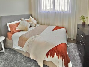 A bed with a striped blanket, pillows, and a bedside table. - Pukehina Retreat: 
Private Pool, Pastures & Beach. (Pukehina)