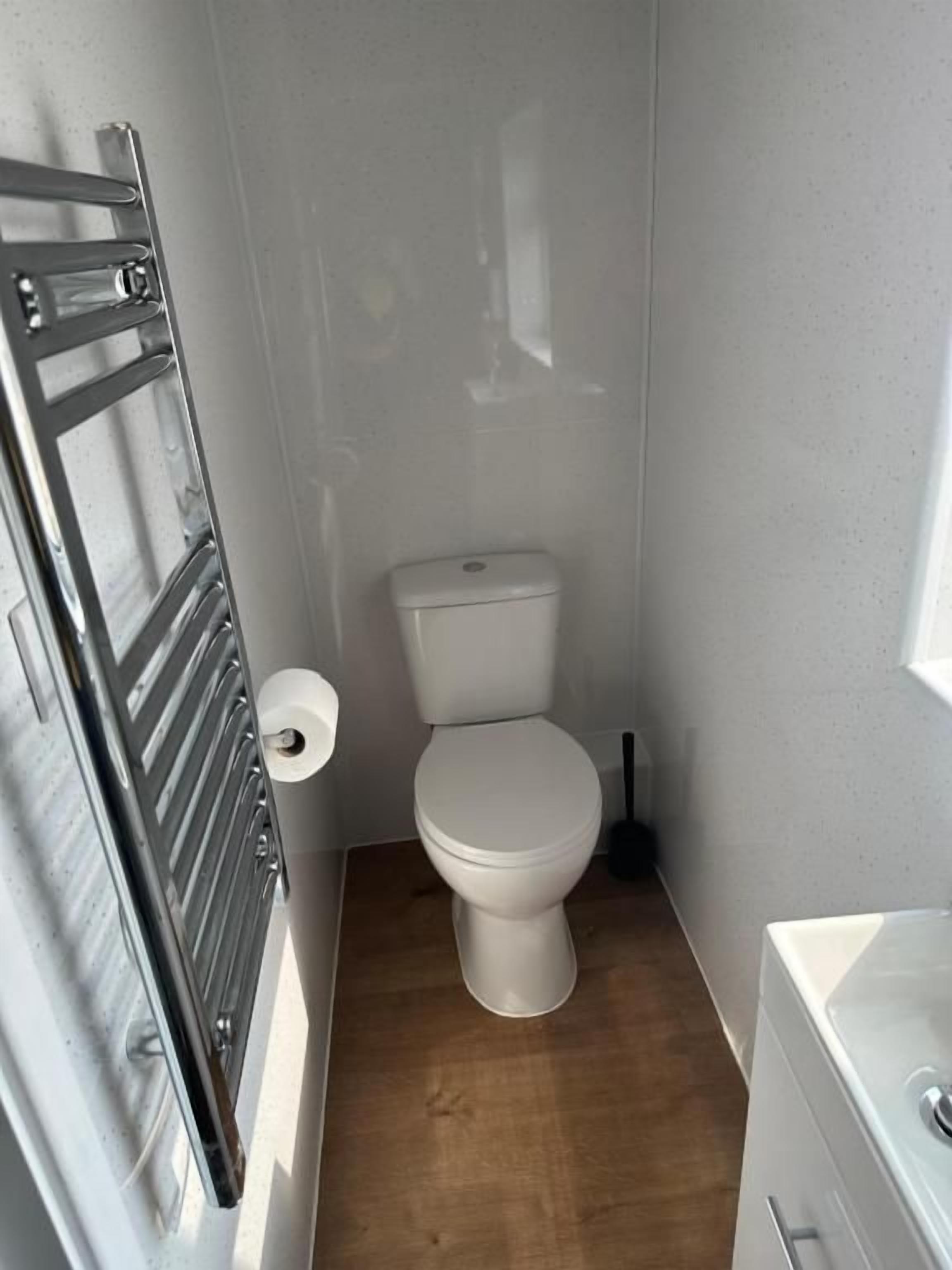 Un baño pequeño con inodoro blanco, suelo de madera y lavamanos blanco.
