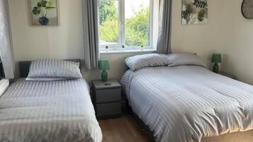 A bedroom with two beds, a window with curtains, bedside tables, and a clock on the wall.