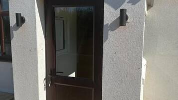 Un edificio con una puerta marrón y una ventana pequeña, rodeado por un muro blanco y un tejado de tejas.