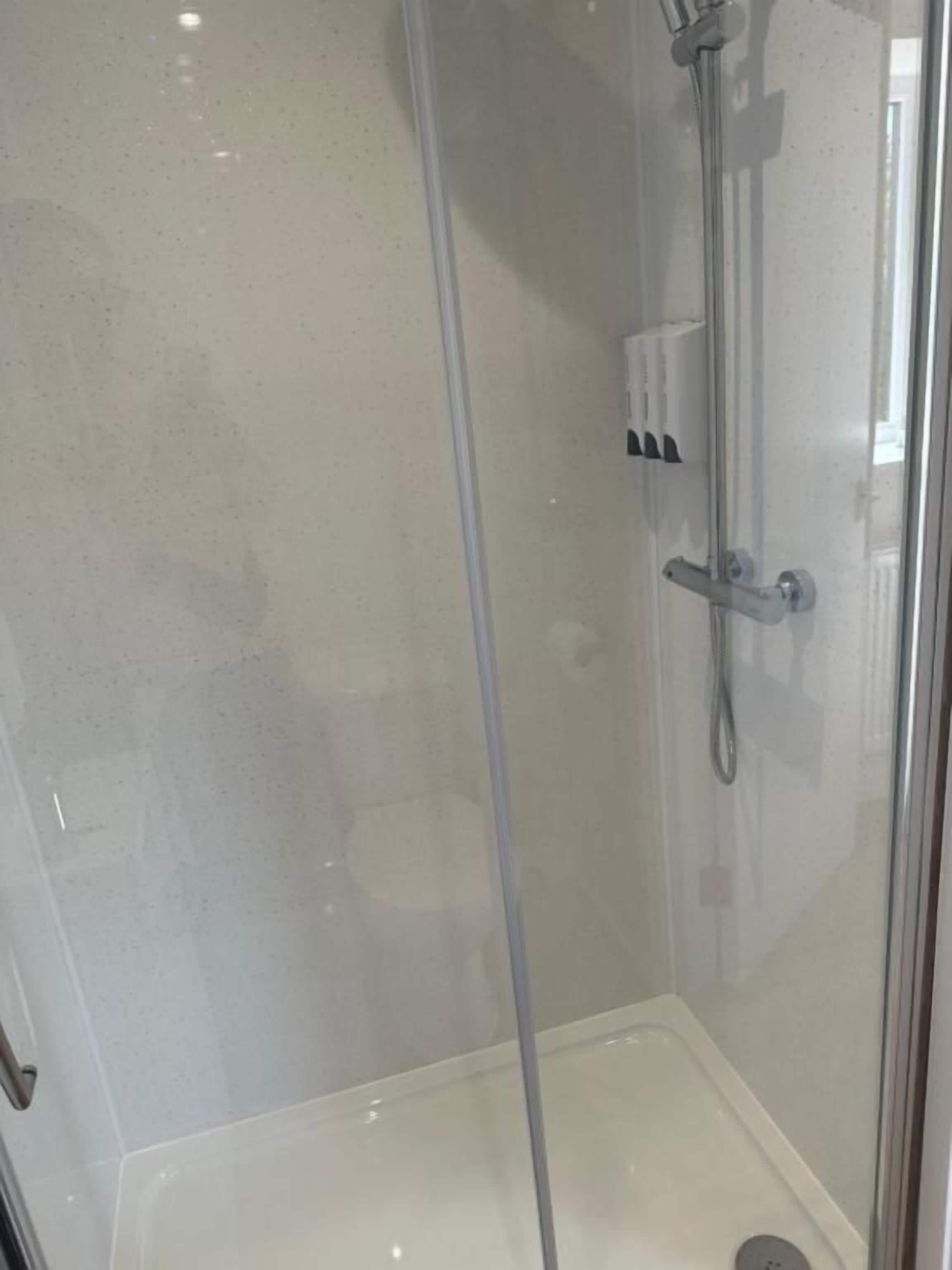 Een douchecabine met glazen wanden, een handdouche en bedieningspaneel.