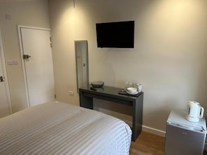 A hotel room with a bed, a desk with a mirror, a television, and a coffee machine.