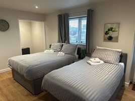 Habitación de hotel con dos camas, un reloj, una ventana con cortinas y una planta en la pared.