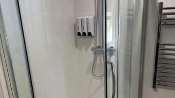 En duschkabin med glasväggar, ett handhållet duschmunstycke, en väggmonterad tvåldispenser och en handdukshängare.