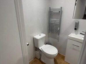 A compact bathroom with a white toilet, a chrome towel rack, and a white sink.