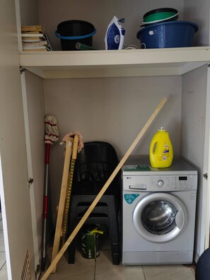 Un espace dédié à la lessive, comprenant un lave-linge, une serpillière, un balai et des produits de nettoyage.