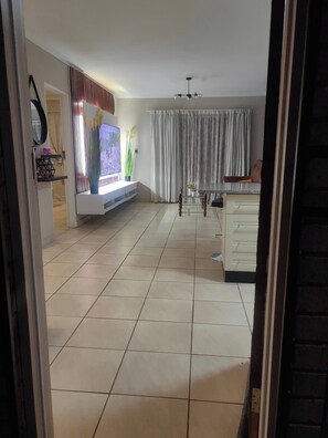 Un salon spacieux doté d’un téléviseur à écran plat, d’un ventilateur de plafond et d’un coin repas avec une table et des chaises.
