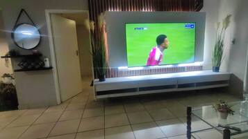 A living room with a flat-screen TV mounted on a wall, a glass coffee table, and a door leading to another room.