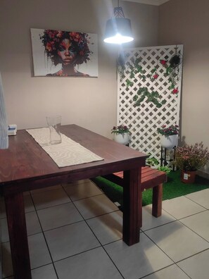 Un coin repas comprenant une table en bois, un banc, une plante en pot et un luminaire fixé au mur.