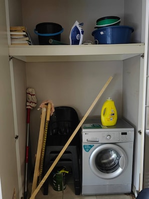 Ein Waschbereich mit Waschmaschine, Mopp, Besen und Reinigungsmitteln.