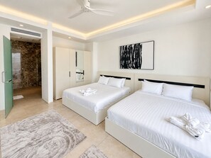 Ein Hotelzimmer mit zwei Betten, einem Deckenventilator, einem Duschbereich mit Marmorfliesen und einem großen abstrakten Gemälde an der Wand.