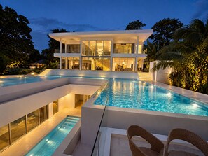 Ein modernes, zweistöckiges Haus mit großem Schwimmbecken und Sitzgelegenheit im Freien.