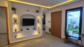 Een moderne woonkamer met een flatscreen televisie, inbouwverlichting en uitzicht op het groen.