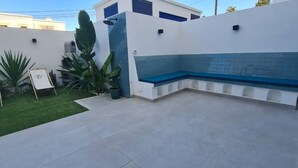 Een terras met een blauwe bank, een kleine tuin met groene planten en een witte muur met een raam.